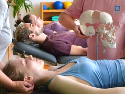 Teilnehmende liegen auf Behandlungsliegen, waehrend Dozent einen Schaedel zeigt und Kopfgriff demon