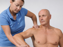 Physiotherapeutin untersucht die Schulter eines sitzenden Patienten, indem sie seinen Arm bewegt un